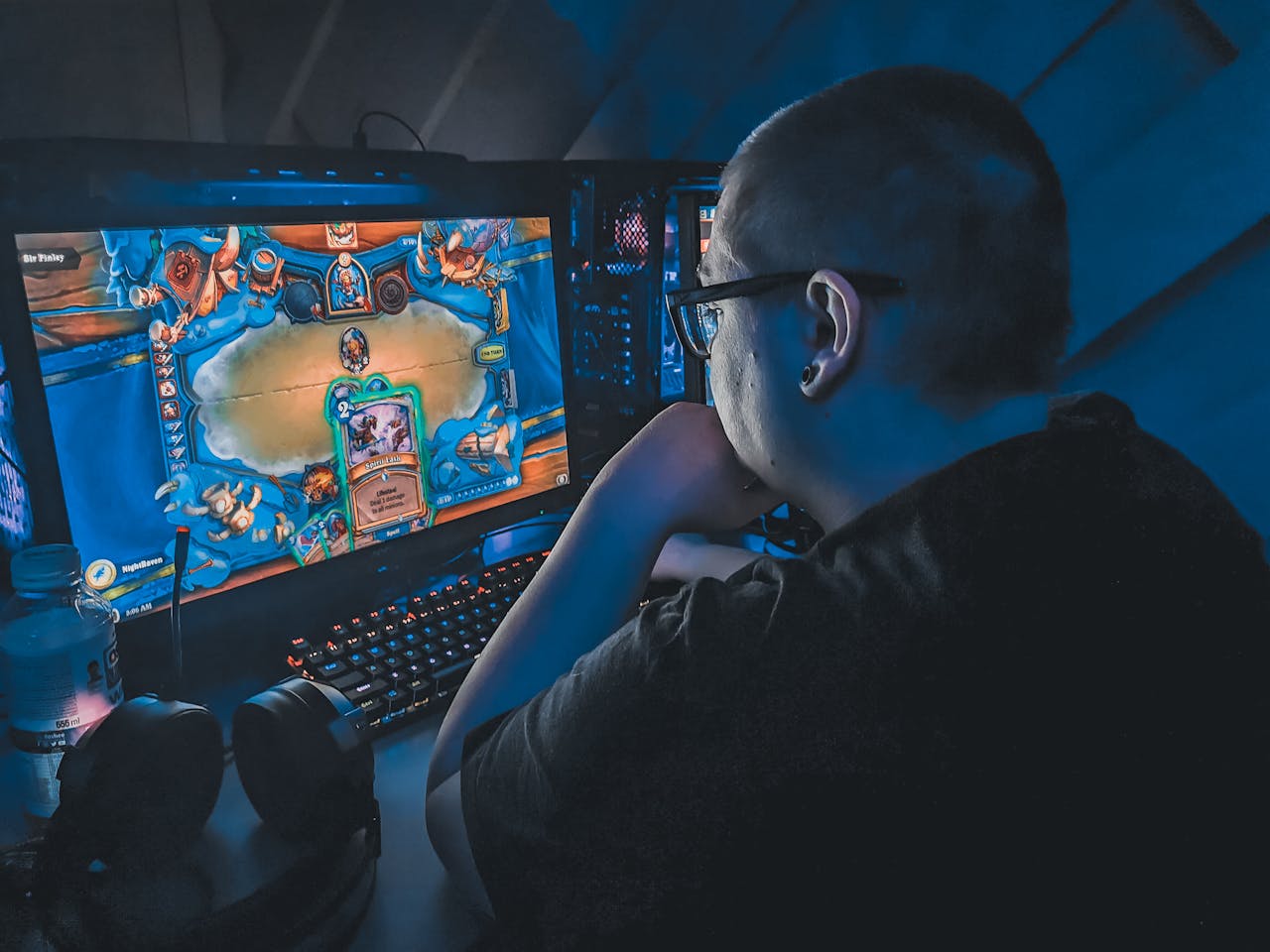 High angle of plump male gamer thinking and playing video game while sitting at table under blue light